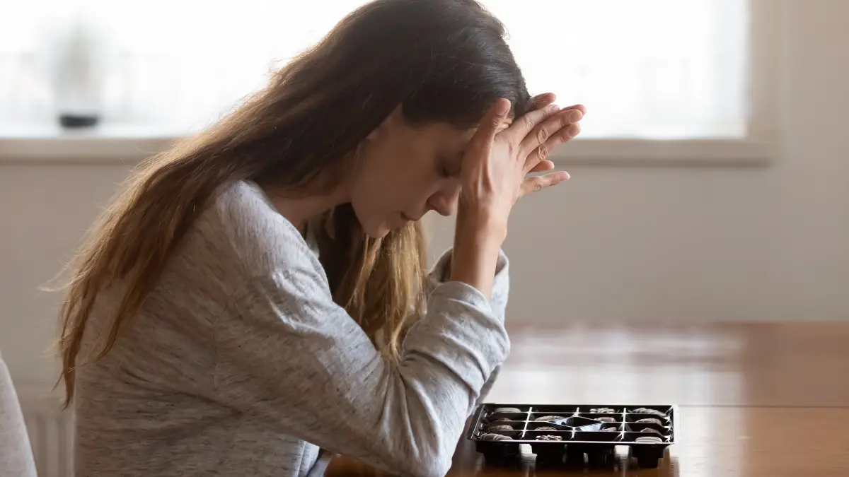 Donna con espressione afflitta seduta davanti a una scatola di cioccolatini, simbolo di disagio legato ai disturbi alimentari